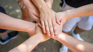 Mehrere Hände von jungen Menschen fassen sich in der Mitte als Symbol für Teamarbeit und Zusammenhalt.